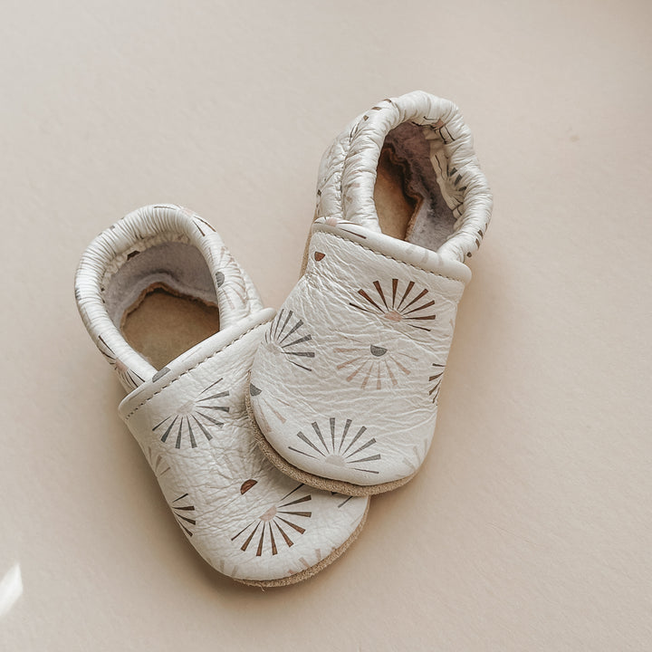 Pretty Please Teether's sunshine print on Caraclarkdesign slip-on shoes. Soft leather. Clay, sage, and beige sunshines on eggshell background