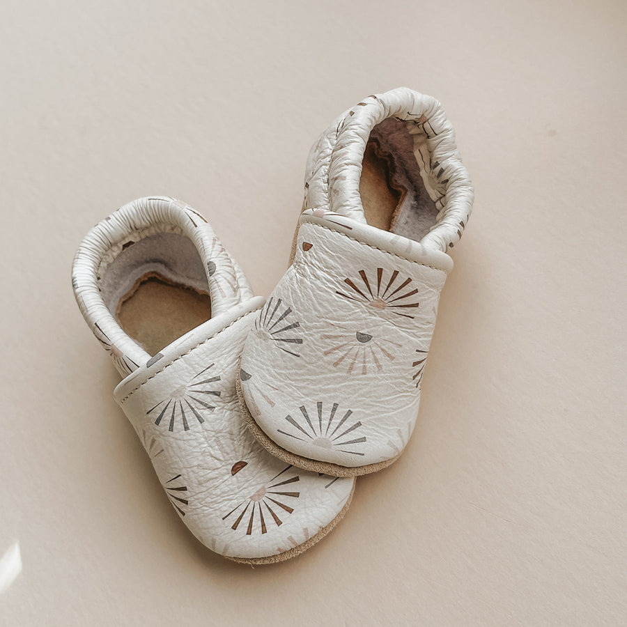 Pretty Please Teether's sunshine print on Caraclarkdesign slip-on shoes. Soft leather. Clay, sage, and beige sunshines on eggshell background